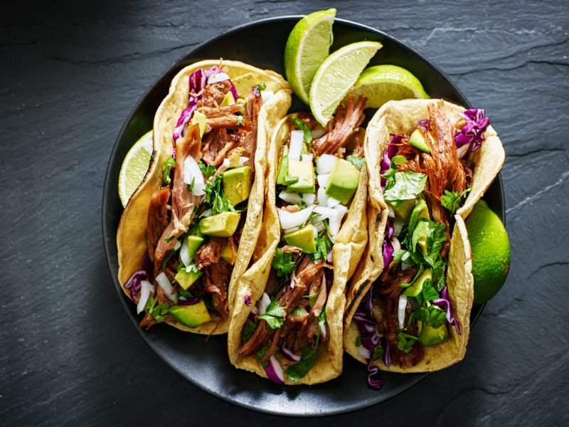 mexican street tacos flat lay composition with pork carnitas, avocado, onion, cilantro, and red cabbage